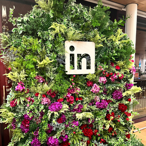 linked in promotional flower wall that is mainly greenery with purple, red and pink flowers